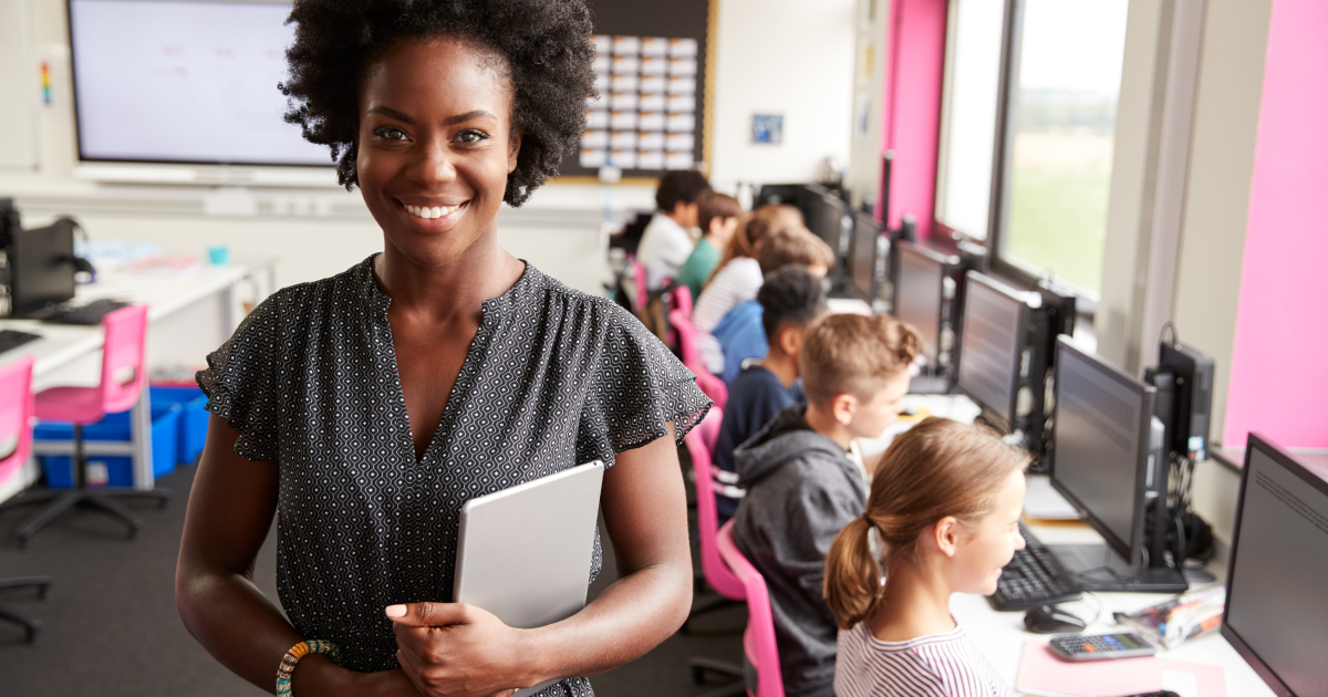 Une enseignante debout dans une salle de classe avec des enfants devant un ordinateur.