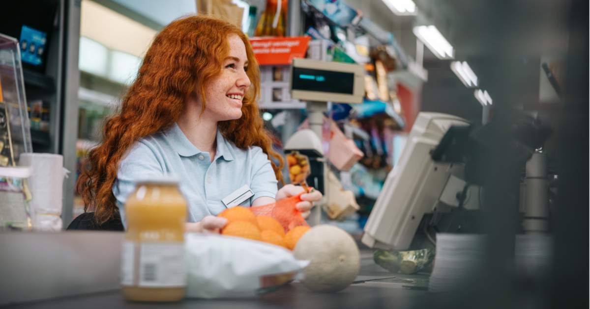 Een bijverdiener die lachend werkt achter de kassa van een supermarkt
