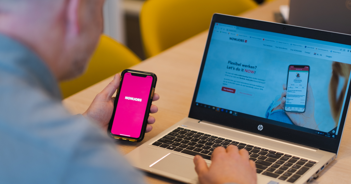 Un homme consultant l'application NOWJOBS via un smartphone et un ordinateur portable